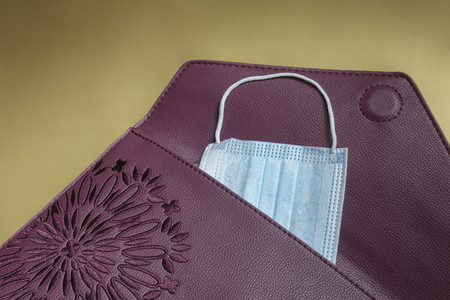 Disposable blue face mask in burgundy clutch purse