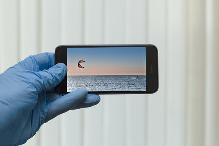 POV Gloved hand looking at kite surfing photo on smart phone screen