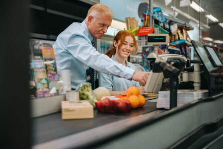 Senior manager training new cashier at supermarket