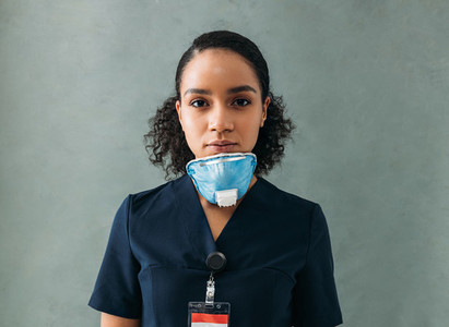 Female doctor with a medical mask under her chin Woman in uniform standing at wall