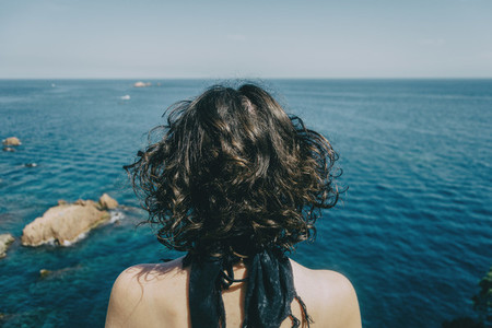 A girl with a kerchief on her neck and her back naked from behind looking at the horizon in the sea