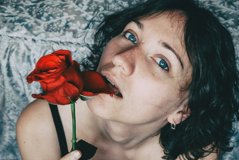 Portrait of blue-eyed beautiful girl biting a petal of a red rose sensually