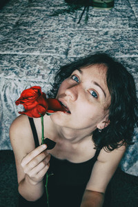 Portrait of blue eyed beautiful girl biting a petal of a red rose sensually