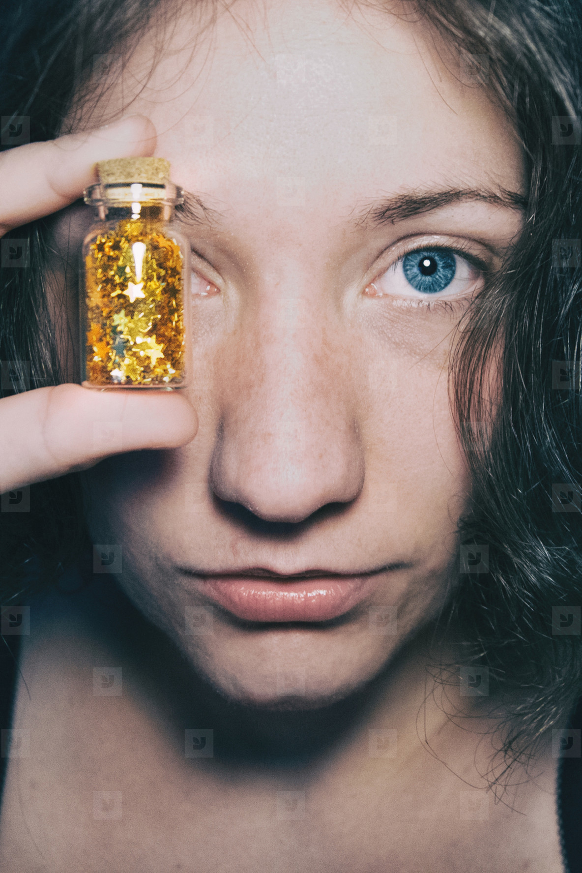 Close up portrait of a blue eyed girl who covers her eye with a bottle full of golden stars
