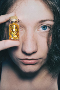 Close up portrait of a blue eyed girl who covers her eye with a bottle full of golden stars