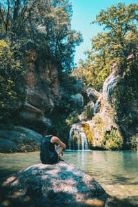 girl sitting on a rock looking at a landscape of a small waterfall