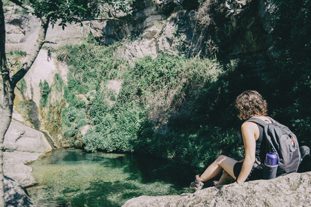 girl sitting on a rock looking at a landscape of a small waterfall