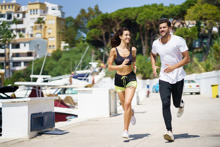 Young couple training together running near the boats in a harbour
