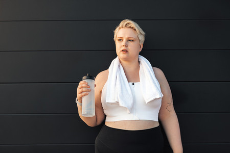 Portrait of a tired curvy woman standing at wall with a towel