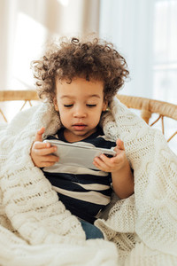 Little boy covered in blanket watching content on a smartphone