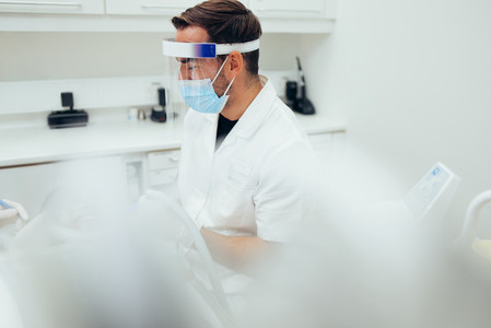 Dentist with face shield examining a patient