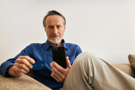 Senior man paying online  Male in casual clothes sitting on sofa holding a credit card