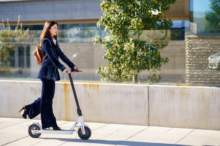 Young business woman wearing blue suit using electric scooter