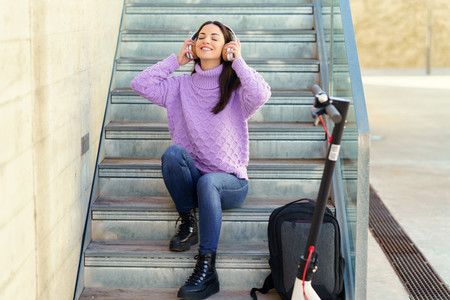 Young woman with electric scooter listening to music with wireless headphones