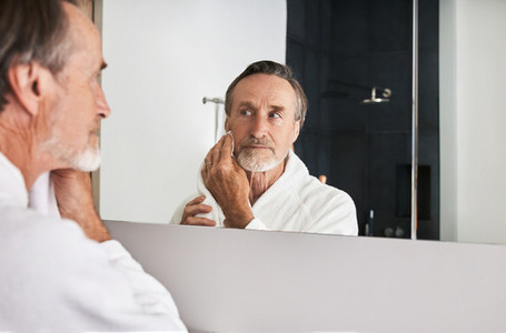 Senior man wiping his face with a towel in front of a mirror