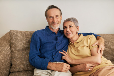 Portrait of smiling senior couple sitting on a couch in a living room Two positive mature people embracing