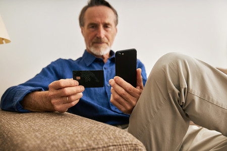 Close up of aged male hands holding a credit card and smartphone  Senior man using payment service at home