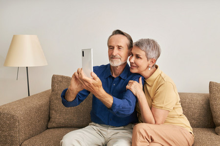 Senior couple spending time at home together  Elderly people taking a selfie while sitting on a couch