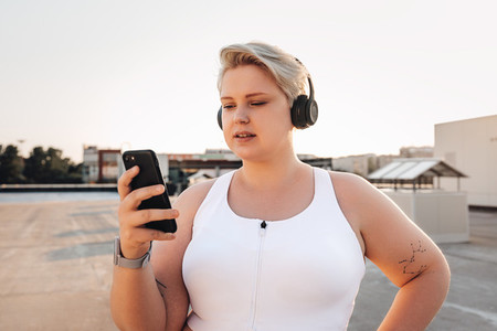 Oversize woman in sports clothes holding a smartphone while standing on the roof at sunset