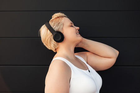 Plus size woman listening to music near a black wall  Young curvy female taking a break during exercises