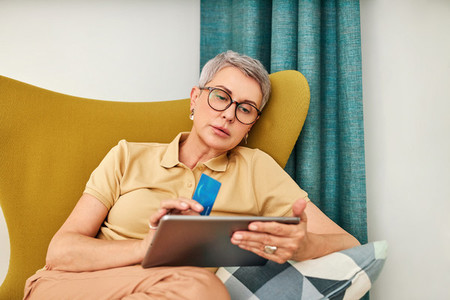 Mature woman in casuals paying by credit card while online shopping from home