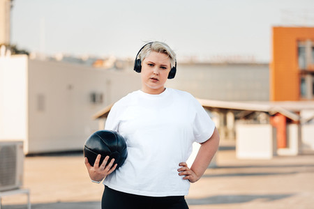 Young woman with plus size body holding a medicine ball while standing on a roof