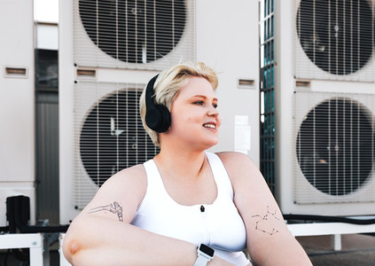 Smiling curvy woman in sportswear sitting on the roof at air conditioning units