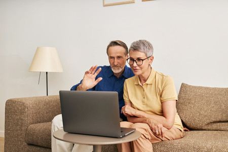 Senior couple using a laptop for video call  Mature man greeting with a hand wave while looking at a laptop
