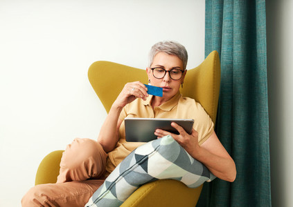 Woman shopping online in living room Mature woman with credit card and digital tablet at home