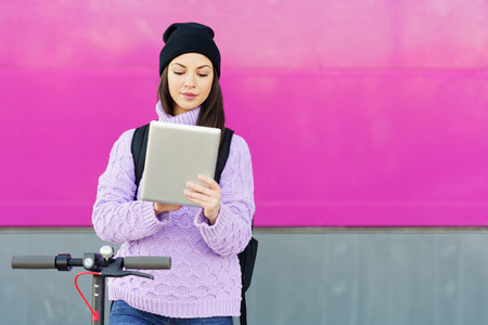 Woman in her twenties with electric scooter using digital tablet outdoors