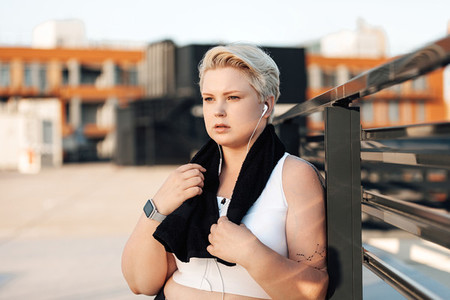 Plus size woman leaning railing on roof  Curvy tired female standing outdoors with a black towel around her neck