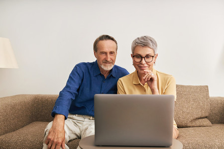 Elderly couple sitting in front of a laptop in a living room communicating during a video call