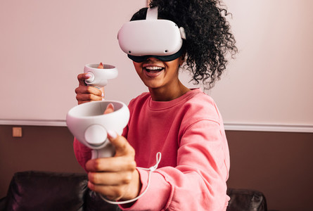 Young smiling woman using VR set while standing in living room  Female in casuals having fun with virtual reality games