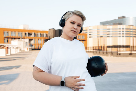 Curvy woman in sportswear holding a medicine ball while standing on roof