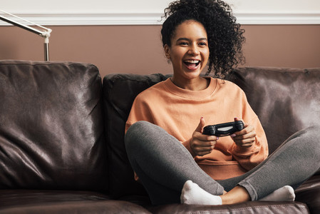 Happy young woman holding a game controller sitting on sofa at home