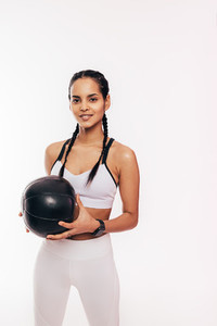 Smiling mixed race woman holding a medicine ball in the studio