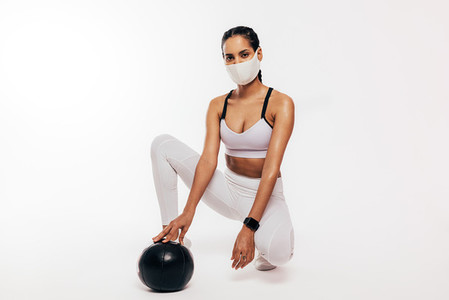 Fitness woman in face mask relaxing after workout with madicine ball