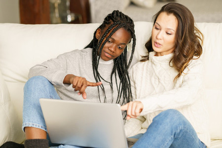 Two female student friends sitting on the couch at home using a laptop