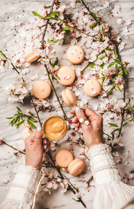 Womans hands holding espresso coffee over macaron cookies and flowers