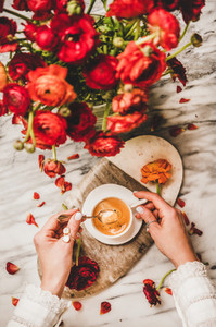 Womans hand holding cup of coffee over red flowers bouquet