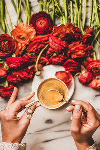 Womans hand holding cup of coffee over table with flowers