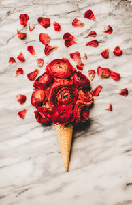 Waffle cone with scoop of ranunculus flowers over marble background