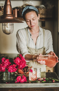 Young woman pouring rose lemonade to glasses in kitchen