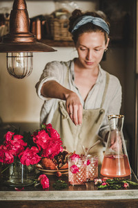 Young woman adding ingredients to glasses with rose lemonade