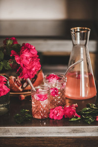 Rose lemonade with ice cubes and petals over kitchen counter