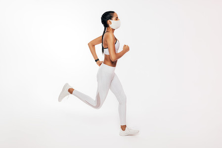 Side view of young fitness woman running over white background wearing a face mask
