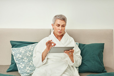 Mature woman with grey hair using a digital tablet in bedroom