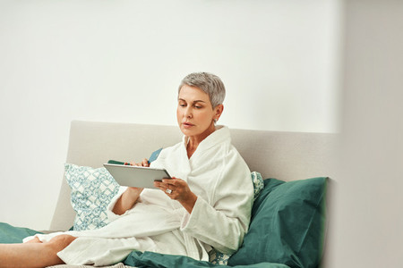 Mature woman relaxing at home  Senior female making online order while lying on a bed