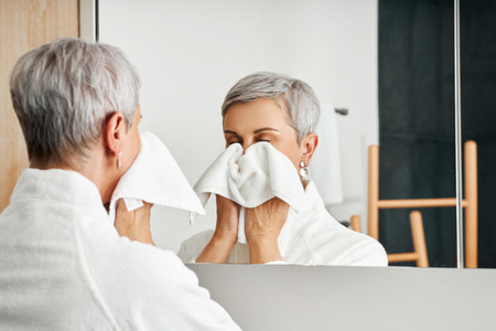 Senior woman wiping face with towel while standing in front of a mirror