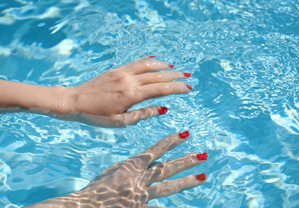 Close up of woman hands with manicure in red under clear pool wa